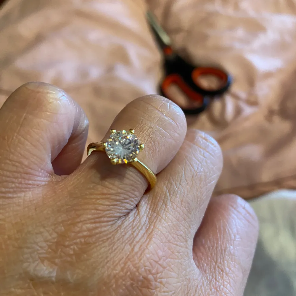 Säljer en elegant guldfärgad  ring med Moissanite  klar sten i mitten. Perfekt för speciella tillfällen eller som en vacker accessoar till vardags. Ringen har en klassisk design med sex klor som håller stenen på plats. Passar perfekt för dig som vill ha något stilrent och tidlöst. . Accessoarer.