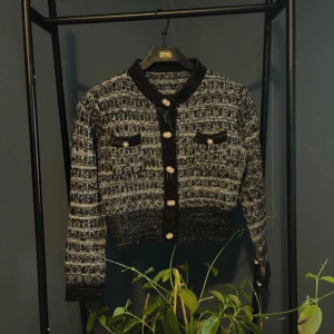 Svart och vit mönstrad kofta - Säljer en snygg svart och vit mönstrad jacka med glittriga knappar. Den har en croppad stil och långa ärmar. Perfekt för höst och vår, och funkar både till vardags och fest. Jackan har två fickor fram och en elegant krage.