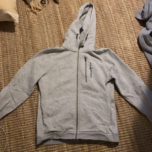 Grå hoodie från Peak Performance - Säljer en grå hoodie från Sail racing i bra skick. Den har en dragkedja framtill och en praktisk huva. Perfekt för kyliga dagar eller som ett extra lager. Passar både till vardags och träning. Storlek 170