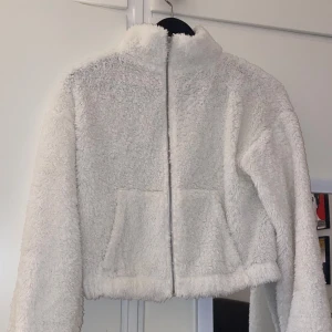Vit teddyjacka med dragkedja - Mysig vit teddyjacka från NLY TREND med dragkedja framtill och två praktiska fickor. Perfekt för kyliga dagar när du vill hålla dig varm och bekväm. Jackan har en hög krage och långa ärmar för extra värme.🤗