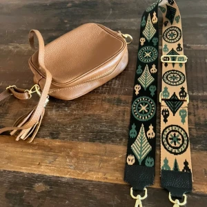 Brun skinnväska med mönstrad axelrem - Säljer en snygg brun skinnväska med en unik mönstrad axelrem i grönt och beige. Väskan har en dragkedja och fransdetaljer. Perfekt för att ge din outfit en bohemisk touch.
