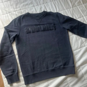 Mörkblå sweatshirt från Woolrich - Säljer en stilren mörkblå sweatshirt från Woolrich med broderad logga på bröstet. Tröjan har långa ärmar och ribbade muddar vid ärmslut och nederkant. Perfekt för en avslappnad stil.