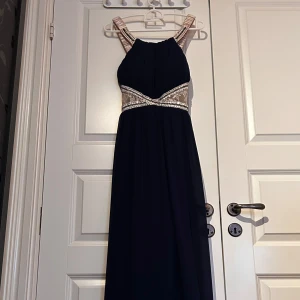 Mörkblå balklänning med pärldetaljer - Elegant mörkblå långklänning med vackra pärldetaljer och spets vid midjan. Klänningen har breda axelband dekorerade med pärlor och paljetter. Obs på ena bandet sticker det ut två trådar anars super fint skick 💙🩵💖storlek s-m