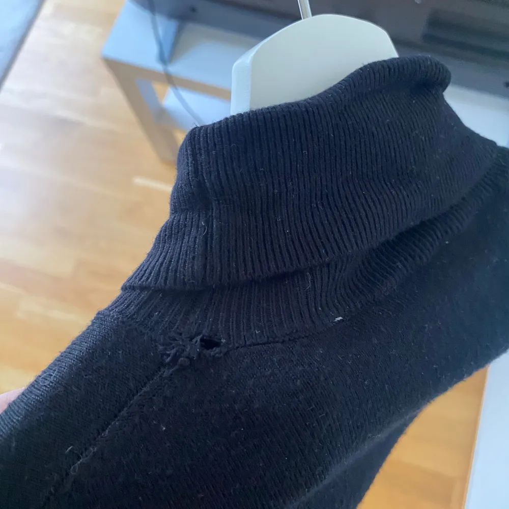 Snygg svart polotröja med långa ärmar och dekorativa knappar vid ärmsluten. Perfekt för kyligare dagar och ger en stilren look. Polokragen ger extra värme och stil. Den har en liten defekt, syns på bild 3.. Neuletakit & Villapaidat.