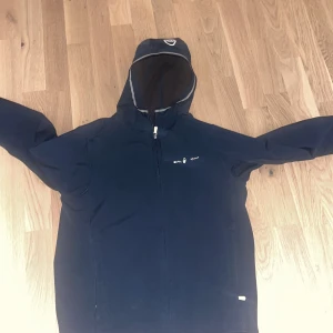 Mörk blå  jacka från Sail Racing - Säljer en svart jacka från Sail Racing med huva och dragkedja. Jackan har en stilren design med logotypdetaljer på bröstet och huvan. Perfekt för kyligare dagar. Jag säljer den för den inte passar och inte kommer till användning längre. Använd Max 10ggr och jackan tvättas innan den skickas iväg. Det bara skriva till mig för mer bilder 