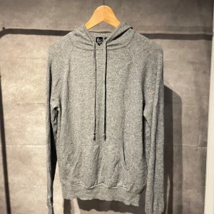 Kashmir hoodie  - Säljer en supermjuk och bekväm grå hoodie i en lyxig blandning av ull och kashmir. Perfekt för kyliga dagar med sin klassiska design och justerbara huva. Den har långa ärmar och en praktisk magficka framtill. Passar perfekt för en avslappnad stil.