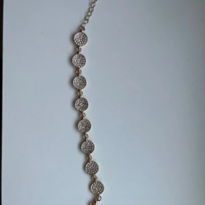 Guldarmband med glittriga detaljer - Elegant guldarmband med runda länkar, varje länk prydd med glittriga stenar. Perfekt för att ge en touch av glamour till din outfit. Justerbar kedja för perfekt passform. Oanvänd. 