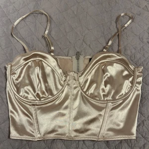 Champagne färgat satin korsett - Snygg champagne färgat korsett i satin med justerbara axelband och dragkedja bak. Perfekt för en stilren look.