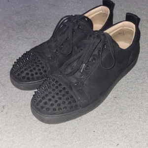 Loubs - Snygga svarta sneakers med nitar på tån och snörning. Skorna har en röd sula som ger en cool kontrast. Perfekta för att ge din outfit en edgy touch.