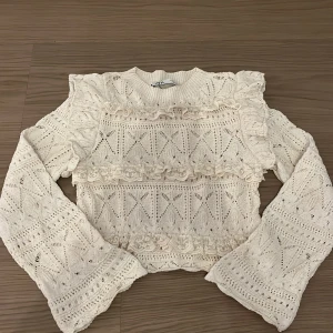 Beige stickad tröja från Zara - Säljer en söt beige stickad tröja från Zara med vackra spetsdetaljer och volanger. Tröjan har ett unikt mönster och långa ärmar, perfekt för skolan och annat. Passar bra till både jeans och kjol. 🌸