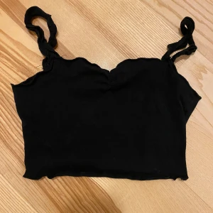 Svart linnetopp/crop top - Svart linne med smala axelband och en enkel design. Kort modell. Strl 146. Passar även XXS - XS.