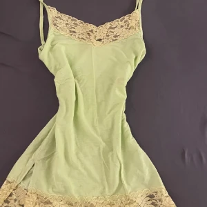 Grön nattlinne med spetsdetaljer - Säljer ett elegant grönt nattlinne med vackra spetsdetaljer i beige vid halsringningen och nederkanten men den har ett hål vid spetsen. Det har smala axelband och en mjuk, bekväm passform. Säljer vidare. Priset kan diskuteras.