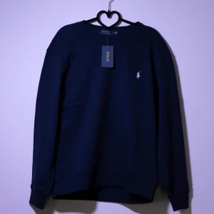 Mörkblå tröja från Ralph Lauren - Säljer en stilren mörkblå tröja från Ralph Lauren med det klassiska logotypbroderiet på bröstet. Tröjan har långa ärmar och en rund halsringning. Perfekt för en avslappnad och snygg look.