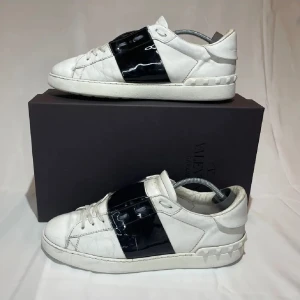 Valentino Open sneakers i vitt och svart - Snygga Valentino Open sneakers i vitt med en bred svart rem över ovansidan. Skorna har en klassisk design med snörning och en bekväm sula. Perfekta för en stilren look. Säljer pga för liten storlek. Skick 8/10