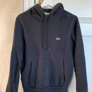 Lacoste Hoodie - Säljer en mörkgrå Hoodie ifrån Lacoste. Mycket fint skick och bara använd fåtal gånger!