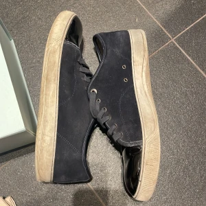 Svarta sneakers från Lanvin - Snygga svarta sneakers från Lanvin med en glansig tå och snörning. Skorna har en robust sula och är tillverkade i mocka med detaljer i syntet. Perfekta för en stilren look. Kommer med snören och påse och box ja kan tvätta dom också storlek 42 men passar upp till 44
