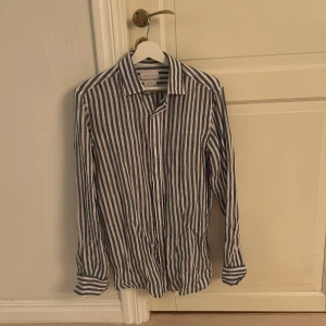 Randig linneskjorta från Massimo Dutti - Snygg randig skjorta från Massimo Dutti i 100% linne. Skjortan har en klassisk krage och knappar framtill. Perfekt för en stilren look med sina blå och vita ränder. Passar bra till både jeans och chinos.