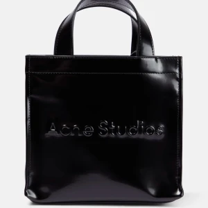 Svart väska från Acne Studios - Snygg svart handväska från Acne Studios i glansigt material. Väskan har ett stilrent och minimalistiskt utseende med märkets logga präglad på framsidan. Perfekt för att ge en touch av elegans till din outfit.