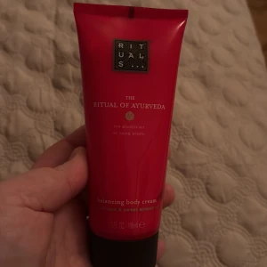 The Ritual of Ayurveda Balancing Body Cream - Säljer en tub av The Ritual of Ayurveda Balancing Body Cream från Rituals. Denna kroppskräm har en härlig doft av indisk ros och mandelolja, perfekt för att återfukta och balansera huden. Kommer i en röd tub med svart lock.