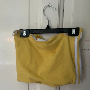 Gula topp från Adidas - Snygg gul topp från Adidas med vita ränder på sidorna och det klassiska Adidas-loggan broderad i vitt. Perfekta för en sportig look.