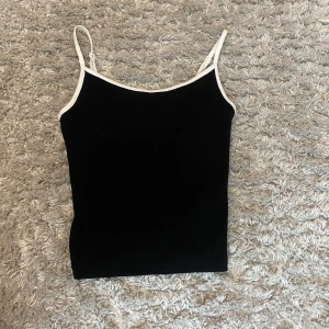 Svart linnetopp från BikBok - Snygg svart linnetopp från BikBok med vita kanter och smala axelband. Perfekt för en stilren look. Toppen är i en enkel och klassisk design som passar till många olika outfits.Pris kan alltid diskuteras🥰