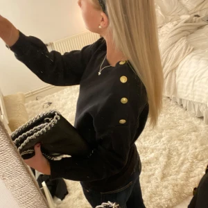 Svart tröja med guldknappar - Snygg svart tröja med dekorativa guldknappar på axeln. Stlk M på lappen men passar också S. (Väskan ligger också ute till försäljning) ❤️