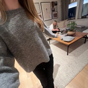 Grå stickad tröja - Säljer en mysig grå stickad tröja med långa ärmar. Perfekt för kyligare dagar och passar till många olika outfits. Tröjan har en avslappnad passform och ribbade kanter vid ärmslut och nederkant.