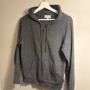 Grå hoodie från Davida - Säljer en stilren grå kashmir hoodie från Davida i storlek S. Den har en dragkedja framtill och en mysig huva. Perfekt för kyliga dagar. Kashmir. Har ett litet hål på armbågen men absolut något som kan enkelt fixas.