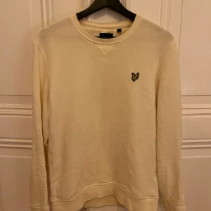 Gulvit tröja från Lyle & Scott - Vit tröja från Lyle & Scott med deras logga på bröstet. Tröjan har långa ärmar och en rund halsringning. 