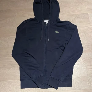 Mörkblå hoodie från Lacoste - Säljer en snygg mörkblå hoodie från Lacoste med dragkedja och huva. Skriv vid minsta fundering🤗