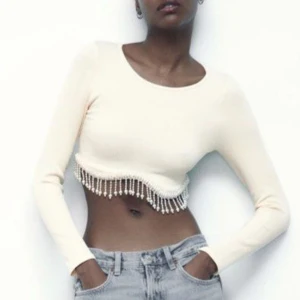 Vit/topp med pärlor Zara - Säljer en superfin vit ribbad croppad topp från Zara. Den har långa ärmar och är dekorerad med pärlor längs nederkanten som ger en extra touch. Perfekt för festival, disco eller konsert😍🌟