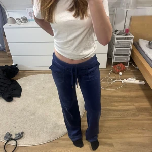 Blå mjukisbyxor från Juicy Couture - Snygga blå mjukisbyxor från Juicy Couture med broderad logga. Byxorna har en bekväm passform med snörning i midjan och praktiska bakfickor med knappar. Perfekta för en avslappnad stil.