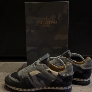 Valentino Rockrunner - Snygga Valentino Garavani sneakers i en cool camouflage-design. Skorna har grå och svarta nyanser med ikoniska nitar runt sulan. Perfekta för att ge din outfit en edgy touch. Skriv för frågor samt funderingar :)