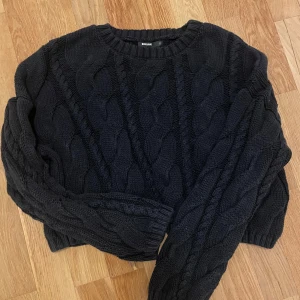 Svart stickad tröja från BikBok - Säljer en snygg svart stickad tröja från BikBok. Tröjan har ett flätmönster och är croppad med långa ärmar. Perfekt för kyligare dagar. 