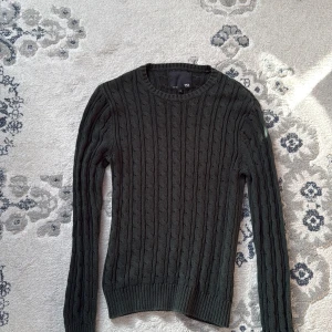 Mörkgrön stickad tröja från 157 - Säljer en snygg mörkgrön stickad tröja från 157. Tröjan har ett klassiskt kabelstickat mönster och långa ärmar. Perfekt för kyligare dagar. Passar bra till både jeans och chinos.