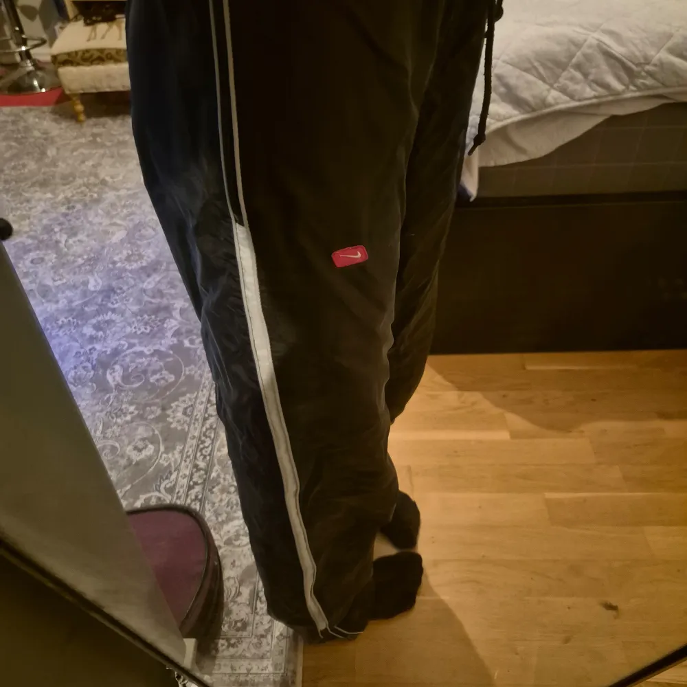 Säljer ett par svarta byxor från Nike med en vit rand längs sidorna. Byxorna har en elastisk midja och en liten röd Nike-logga på sidan💞💕. Jeans & Byxor.