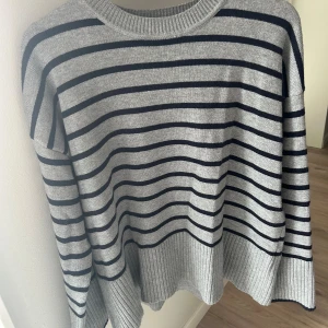 Grå och svart randig tröja från Zara - Säljer en supermysig grå tröja från Zara med svarta ränder. Den är stickad och har en normal passform med långa ärmar. Perfekt för höst och vinter när du vill hålla dig varm och stilren. Tröjan är i bra skick och redo för en ny ägare!