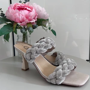 Glittriga sandaler med flätad rem - Säljer ett par eleganta sandaler med glittriga flätade remmar. De har en fyrkantig tå och en bekväm klack, perfekta för festliga tillfällen. Sandalerna är i nyskick och har en stilren design som passar till både klänning och byxor.
