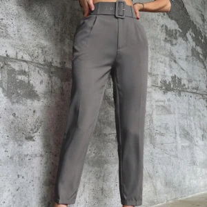 Grå kostymbyxor med bälte - Snygga grå kostymbyxor med hög midja och ett matchande bälte. Byxorna har en rak passform och är perfekta för både kontoret och mer formella tillfällen. De är tillverkade i ett bekvämt material som ger en stilren look.