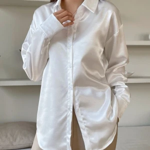 Vit satinblus - Säljer en superfin vit blus i satinmaterial. Den har en klassisk krage och knappar hela vägen ner. Perfekt för både vardag och fest! Den är långärmad och har en lös passform som ger en avslappnad men stilren look.