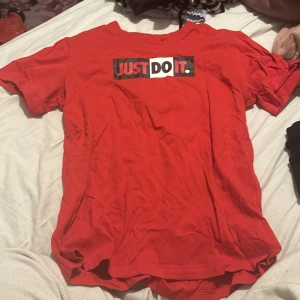 Röd Nike T-shirt med 'Just Do It' tryck - Säljer en röd Nike T-shirt i storlek S med det klassiska 'Just Do It' trycket på framsidan. T-shirten är kortärmad och gjord i mjukt bomullsmaterial, perfekt för vardagsbruk eller träning. Den är i bra skick och redo för en ny ägare!