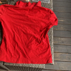 Röd pikétröja från Lacoste - Säljer en snygg röd pikétröja från Lacoste. Den har korta ärmar och klassisk krage med knappar. Perfekt för en casual look eller en dag på golfbanan. Tröjan är i bra skick och redo för en ny ägare!