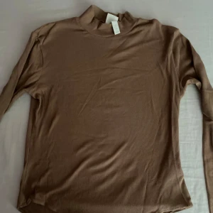 Brun ribbad bodysuit - Säljer en snygg brun ribbad bodysuit med långa ärmar. Perfekt för höst och vinter, den är både stilren och bekväm. Passar bra till både vardag och fest!