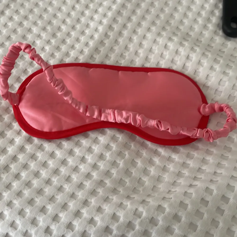 Supergullig rosa sovmask med röda hjärtan. Den har en elastisk rem som är täckt med rosa tyg för extra komfort. Perfekt för en god natts sömn eller en mysig tupplur!. Accessoarer.