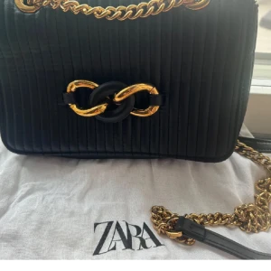 Svart quiltad axelväska från Zara - Säljer en ny superfin svart quiltad axelväska från Zara. Väskan har en elegant kedja i guld och en snygg detalj framtill. Perfekt för både vardag och fest! 🖤tygpåse tillkommer med..!