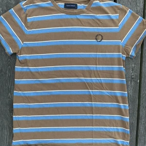 Randig Tshirt - Randig Tshirt i nougatbrun/blå/vit med brodyr: Clean Cut Copenhagen Använd men bra kvalité. 