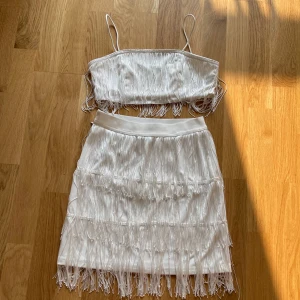 Vit fransig tvådelad klänning - Säljer en superfin vit tvådelad klänning med fransar. Toppen har tunna axelband och kjolen är kort med flera lager av fransar som ger en härlig rörelse. Perfekt för fest eller en somrig dag ute! 🌟