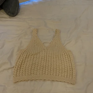 Beige stickad topp från H&M - Säljer en superfin beige stickad topp från H&M. Den är ärmlös och har en v-ringad design med breda axelband. Perfekt för en avslappnad sommarlook eller att ha under en kavaj för en chic stil. Toppen är i nyskick och väldigt bekväm att bära.