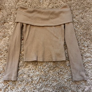 Beige ribbad offshoulder topp - Säljer en superfin beige ribbad offshoulder topp. Den är perfekt för både vardag och fest med sin stilrena design. Toppen har långa ärmar och en bekväm passform. Passar perfekt till jeans eller kjol!