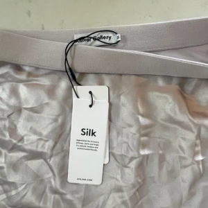 Silvrig sidenkjol från Anivar Gallery - Säljer en elegant och lyxig silvrig kjol i siden från Anivar Gallery. Kjolen har en mjuk och glansig yta som ger en exklusiv känsla. Perfekt för festliga tillfällen eller när du vill känna dig extra fin. Den har en bekväm passform och är lätt att matcha med olika toppar.